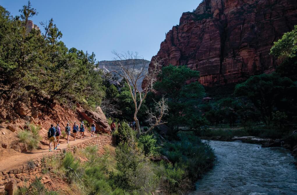 Students walk along a trail in a small canyon with a river flowing not far below them